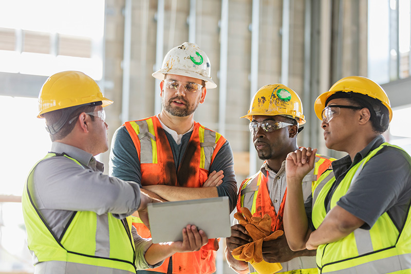 One construction worker giving a presentation around a clipboard to three other construction workers