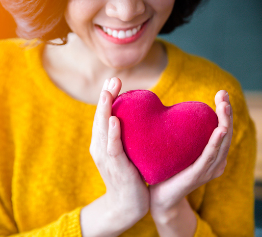 a women in a yellow sweater holding a red heart