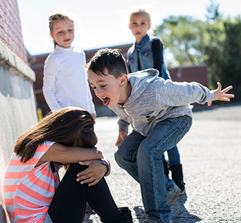 young girl sitting against the wall crying while getting bullied by three other kids.