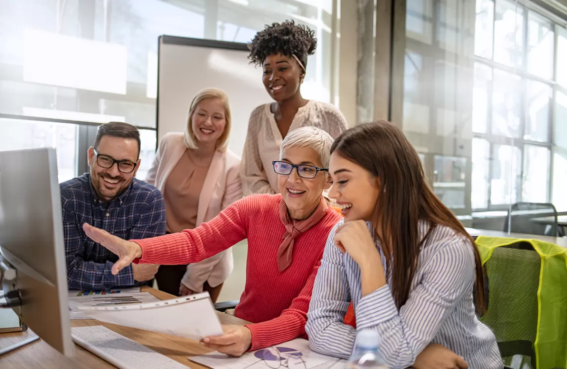 A diverse group of people gathered around a computer. 