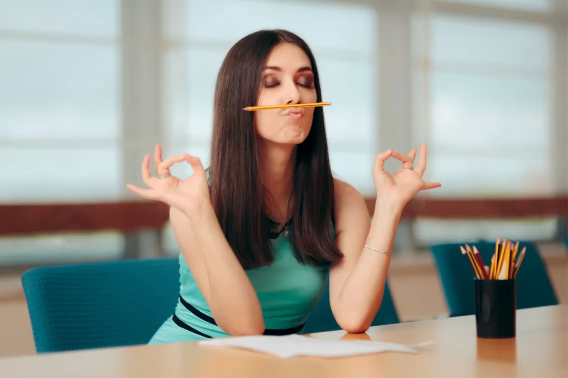 Woman "meditating" at a desk while holding a pencil between her lips and nose