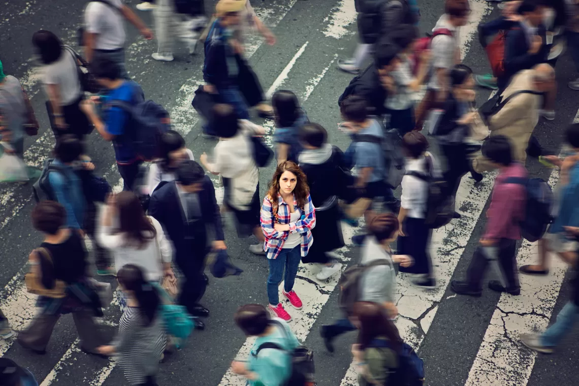 One person in focus, looking at the camera, in a busy cross walk, many other people walking by out of focus