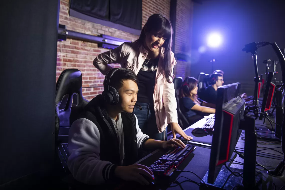 a female esports coach watching and helping a male gamer