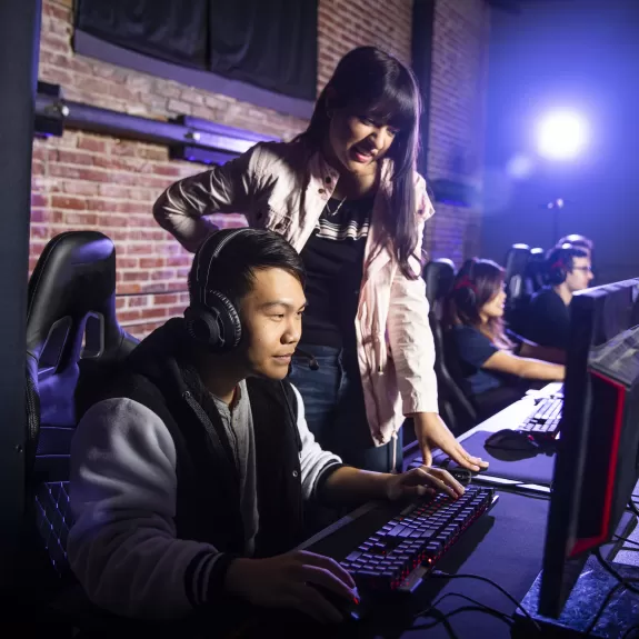a female esports coach watching and helping a male gamer