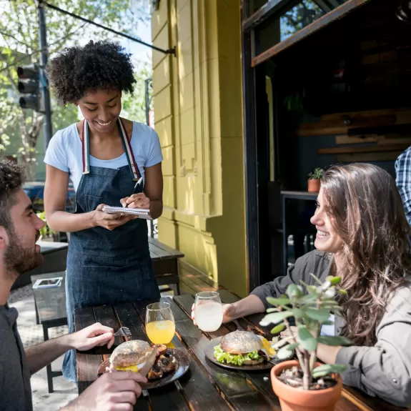 Waitress taking the order of two people sitting outdoors at a restaurant 